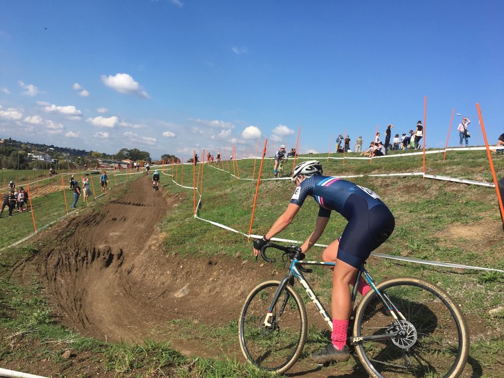 Cyclist racing a cyclocross event on a dirt course with spectators in the background