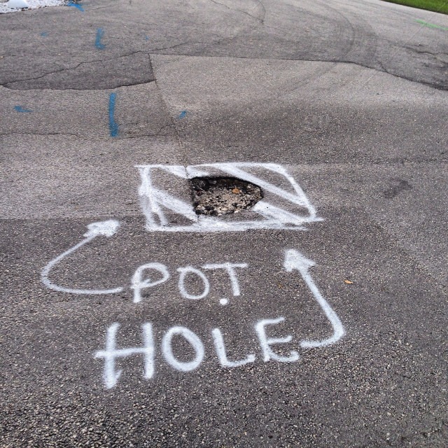 Pothole marked on a road surface with spray paint and arrows pointing around it