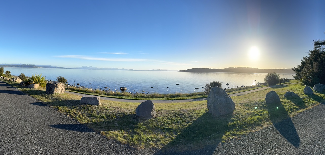 Wide coastal landscape with walking path, rocks, and sunlight over calm water, illustrating natural environments linked to mental health