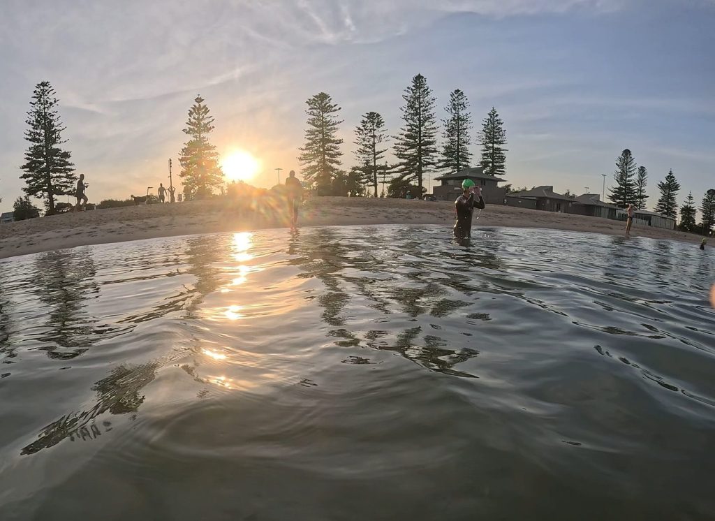 Water-level view of people swimming in calm ocean at sunset, illustrating swimming and nervous system regulation