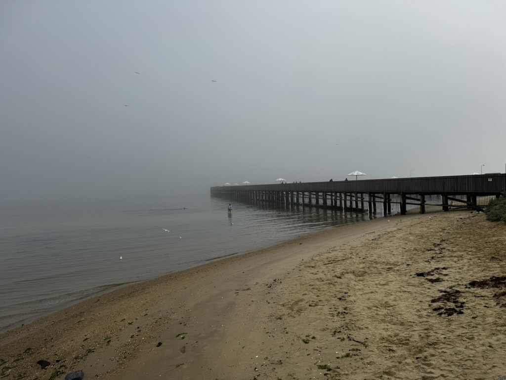 Pier extending into calm water on a foggy morning.