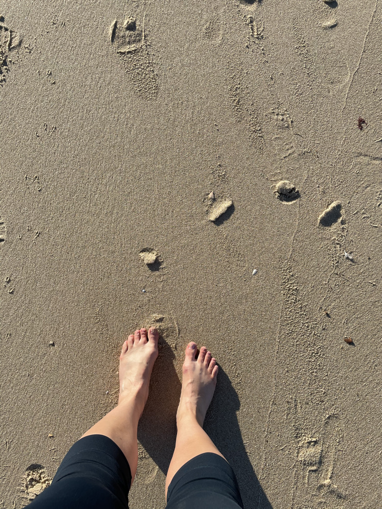Feet standing on wet sand at the edge of the beach, capturing a calm moment of grounding.