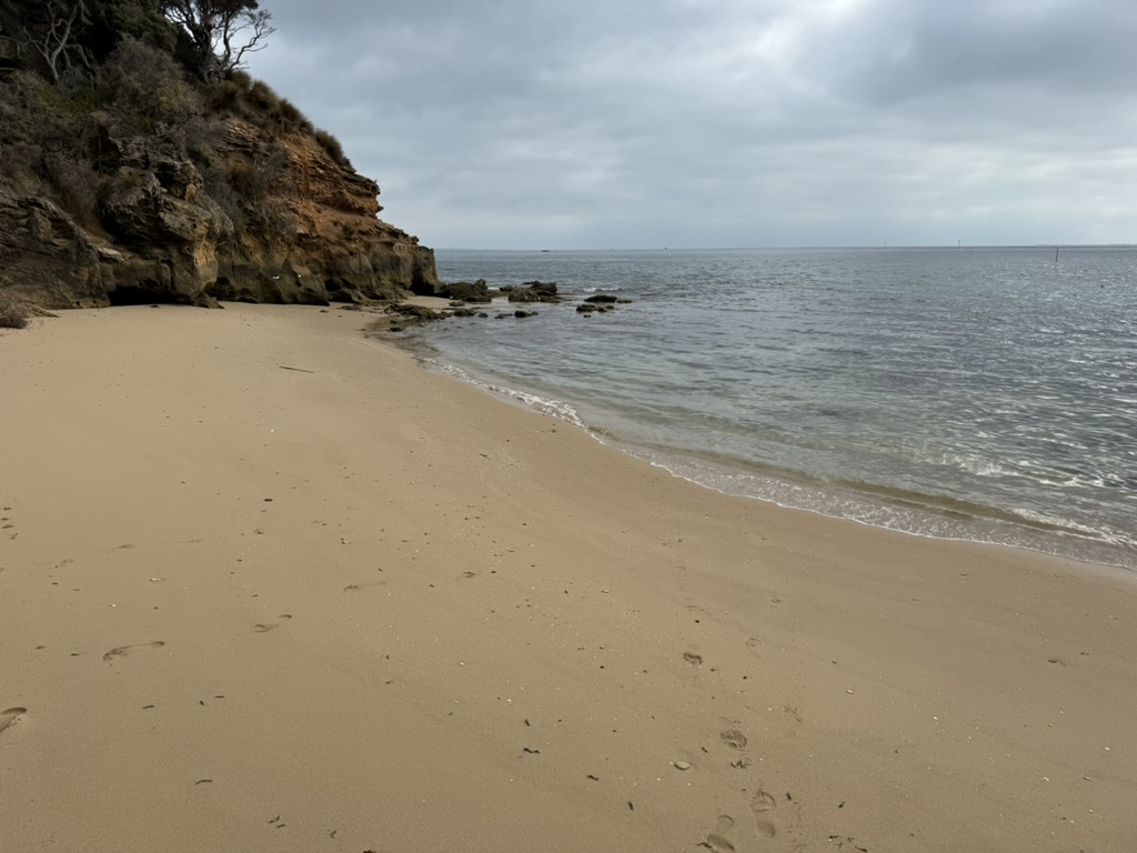 Quiet sandy cove with gentle waves and a rocky shoreline under a soft, overcast sky