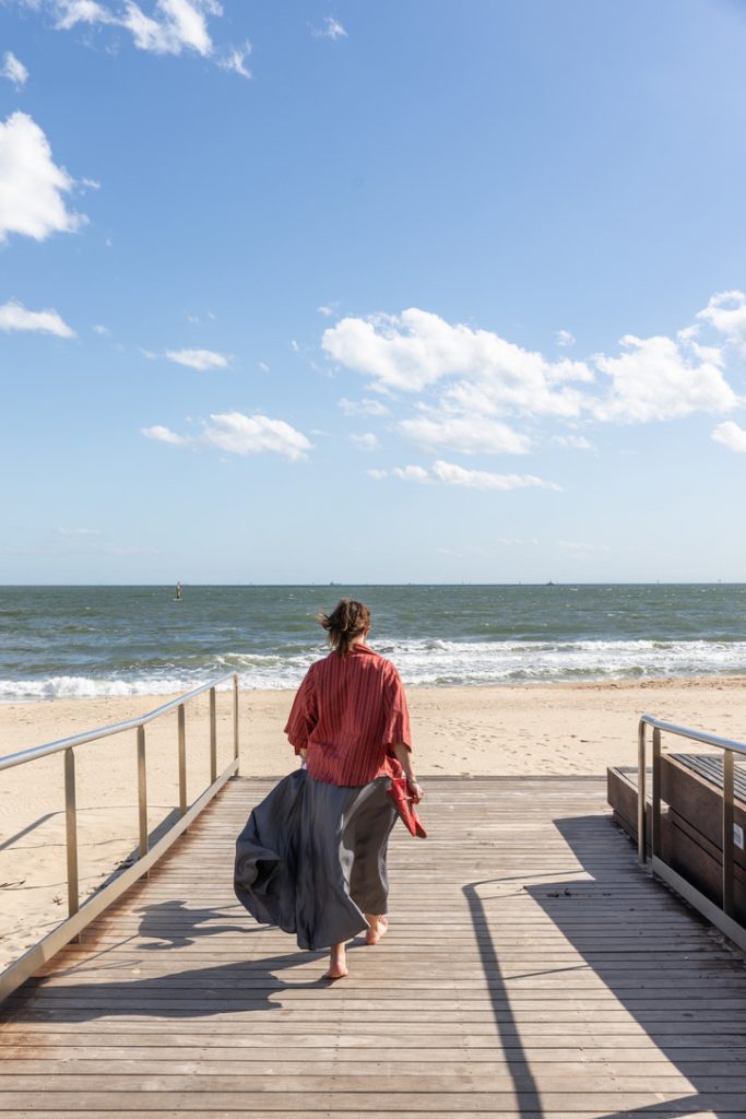 Person walking along a wooden path toward the ocean, representing moving forward with discomfort and psychological flexibility