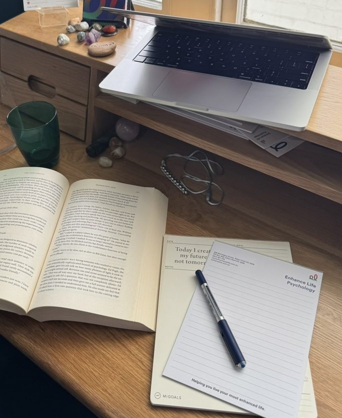 Open book, notebook and laptop on a desk by a window, representing deep reading and reflective thinking