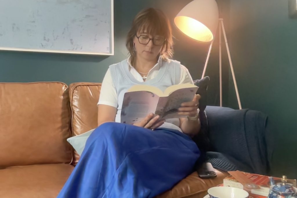 Nonie Carr reading a book on a couch, representing deep reading and focused attention