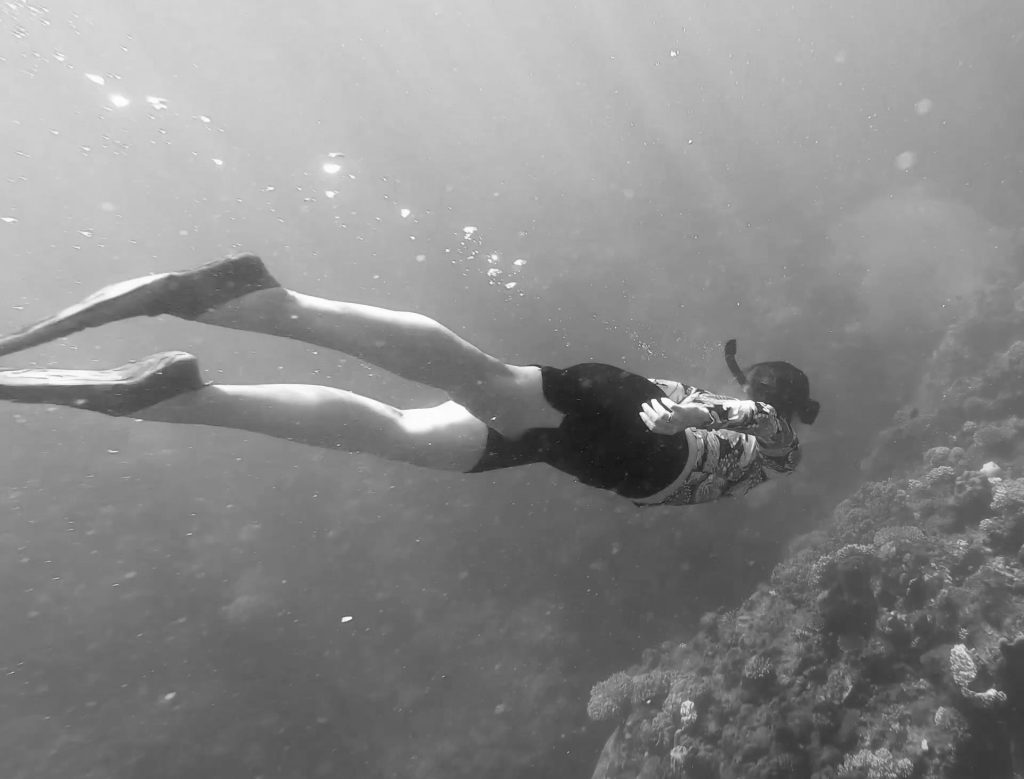 Black and white image of a person swimming underwater, representing focused attention and movement