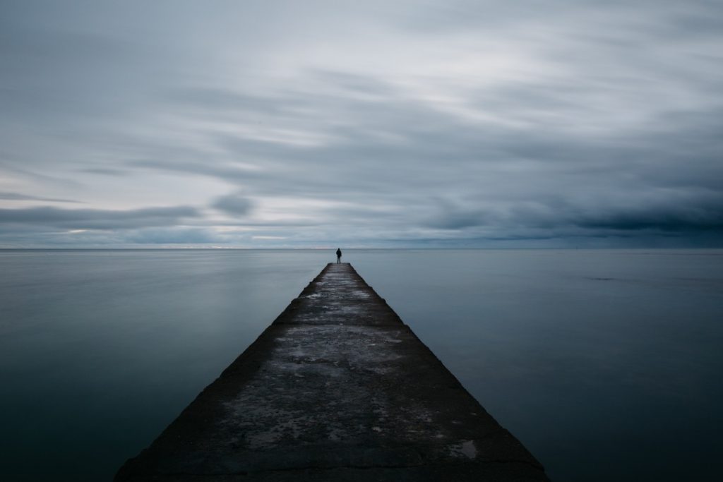 Jetty extending into calm water with a distant figure, representing focus and direction