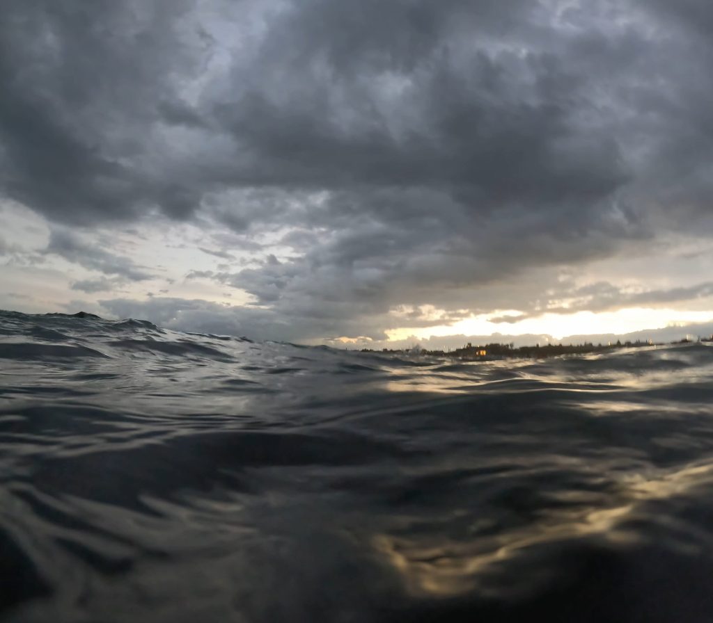 Heavy, shifting cloud with light breaking through low on the horizon, seen from the water over an uneven sea surface.