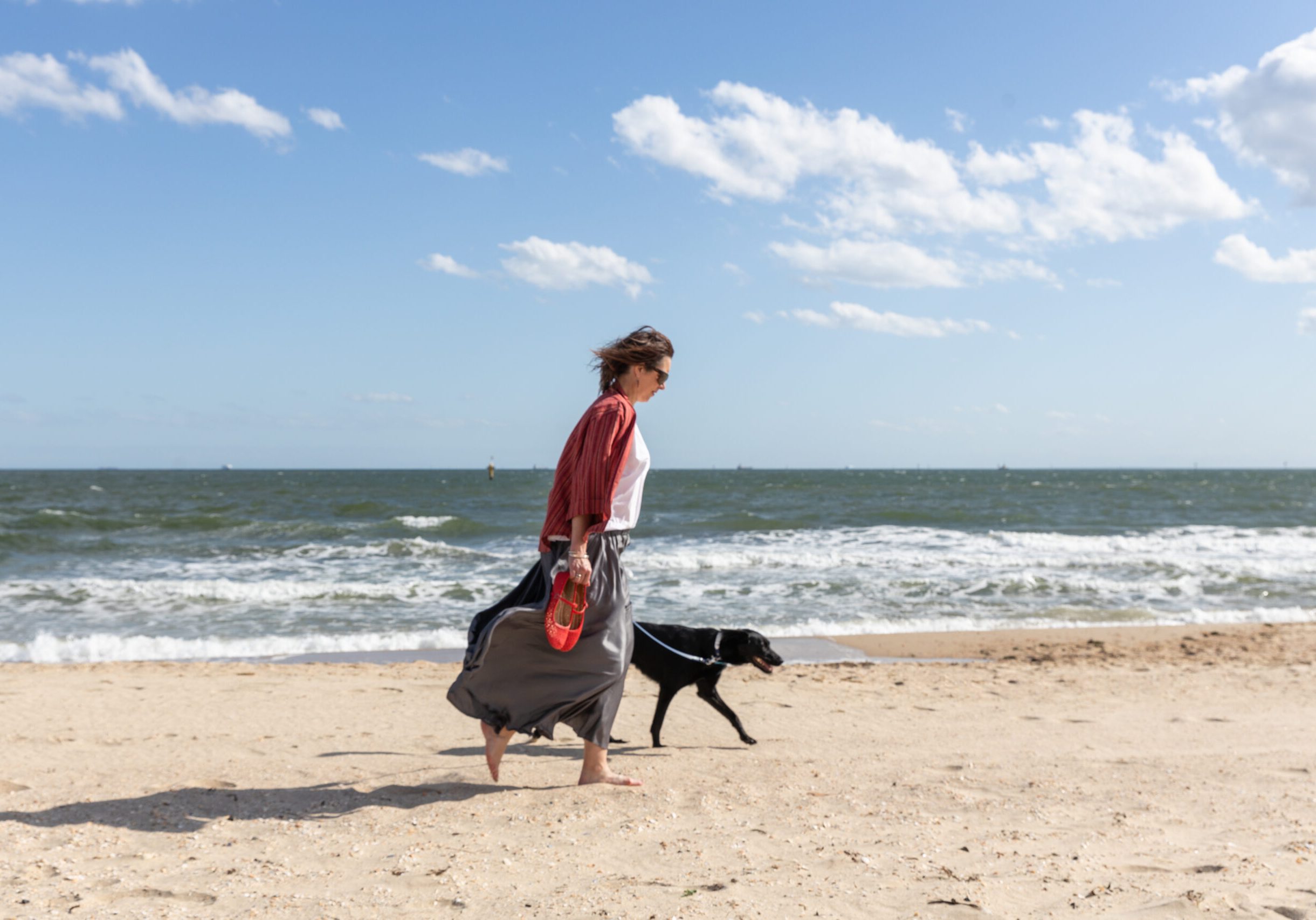 Psychologist Nonie Carr walking on the sand at the beach with Bindi the black kelpie, sharing a calm moment by the ocean